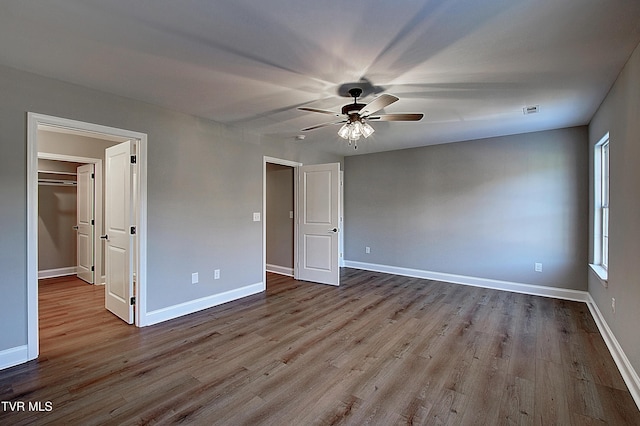 unfurnished bedroom featuring light wood-type flooring, ceiling fan, a spacious closet, and multiple windows