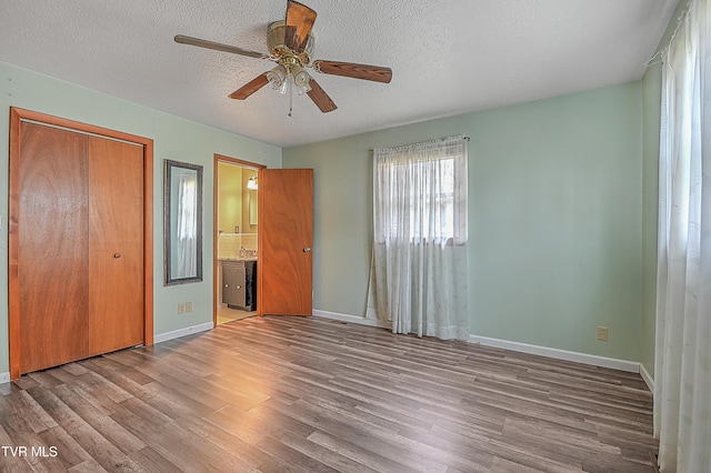 unfurnished bedroom with light wood-type flooring, a textured ceiling, ceiling fan, connected bathroom, and a closet