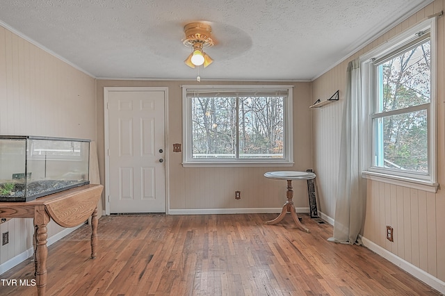 foyer featuring wood walls, ceiling fan, ornamental molding, a textured ceiling, and wood-type flooring