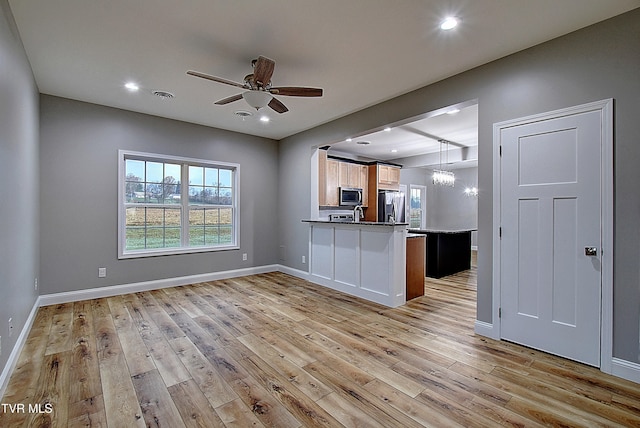 kitchen with hanging light fixtures, stainless steel appliances, kitchen peninsula, ceiling fan with notable chandelier, and light wood-type flooring