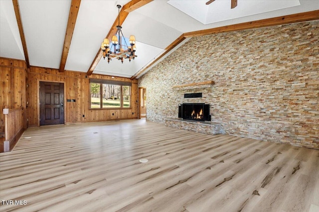 unfurnished living room with a stone fireplace, light hardwood / wood-style flooring, beamed ceiling, wood walls, and ceiling fan with notable chandelier