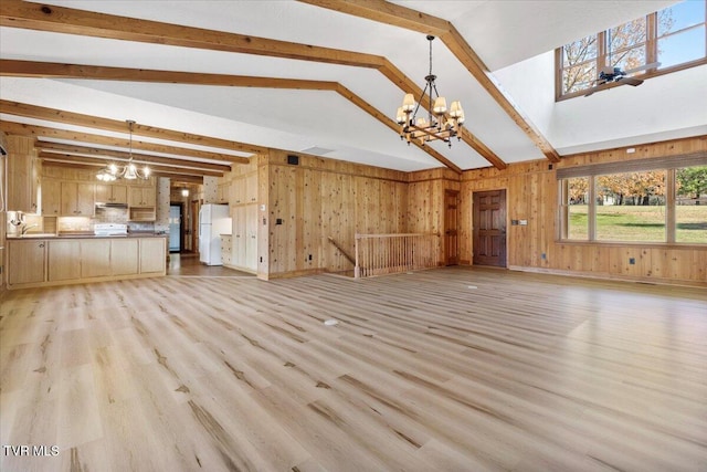 unfurnished living room featuring beam ceiling, light hardwood / wood-style flooring, a notable chandelier, and wood walls