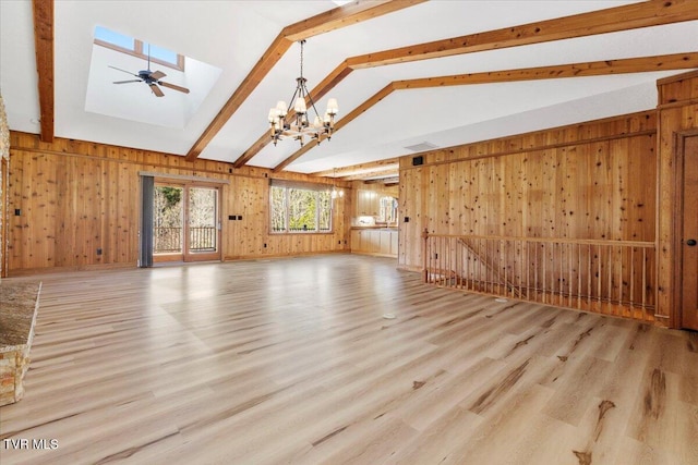 unfurnished living room with ceiling fan with notable chandelier, light hardwood / wood-style floors, wood walls, and vaulted ceiling with skylight