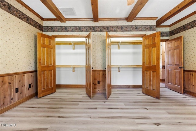 interior space featuring beam ceiling, wood walls, a closet, and light hardwood / wood-style floors