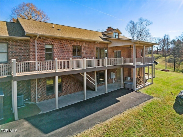 rear view of house featuring central air condition unit, a wooden deck, a patio area, and a lawn