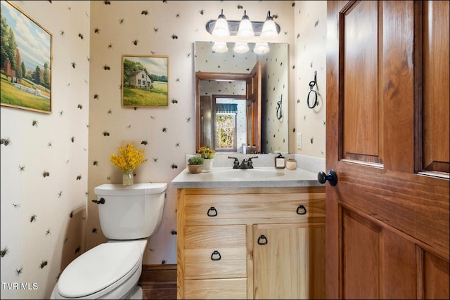 half bath featuring wallpapered walls, toilet, and vanity