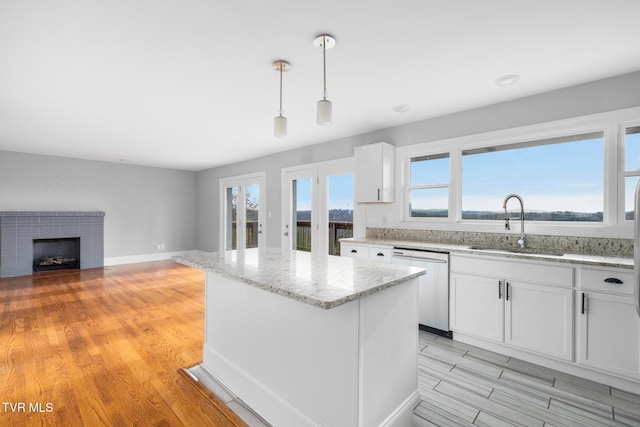 kitchen featuring dishwasher, hanging light fixtures, a fireplace, white cabinets, and light wood-type flooring