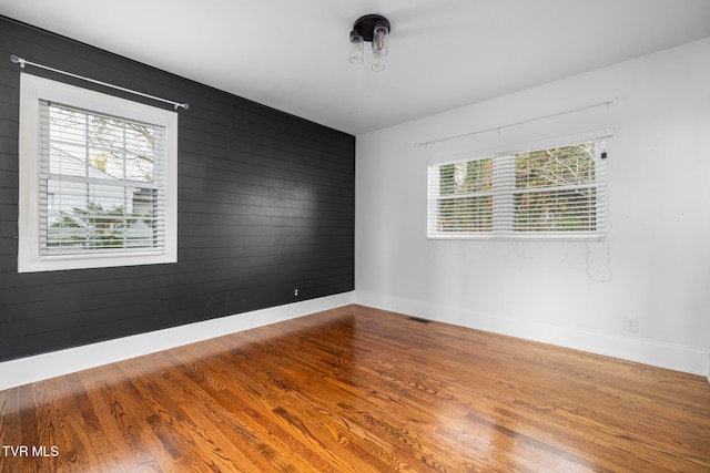 unfurnished room featuring hardwood / wood-style flooring, a healthy amount of sunlight, and wood walls