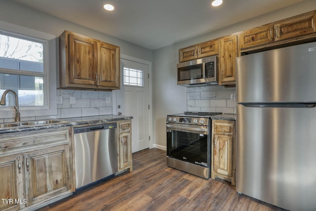 kitchen featuring a sink, appliances with stainless steel finishes, decorative backsplash, and dark wood-style flooring