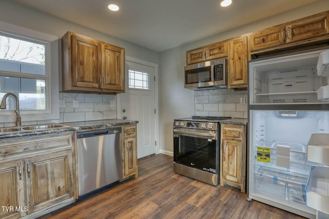 kitchen featuring stainless steel appliances, dark wood-type flooring, a sink, brown cabinets, and tasteful backsplash