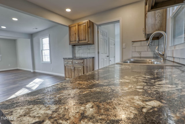 kitchen with baseboards, decorative backsplash, brown cabinets, dark wood-type flooring, and a sink