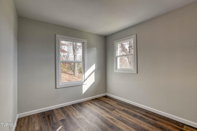 empty room with dark wood-style floors, plenty of natural light, and baseboards