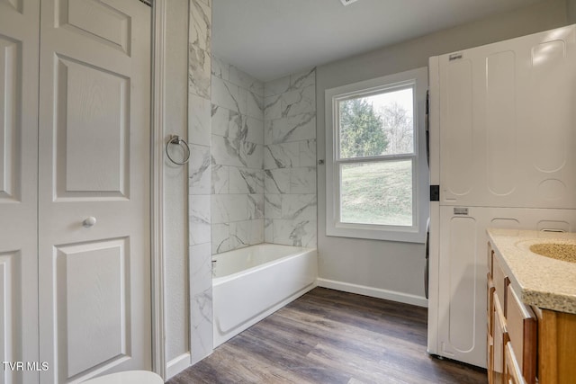 bathroom with stacked washer / drying machine, vanity, shower / tub combination, wood finished floors, and baseboards