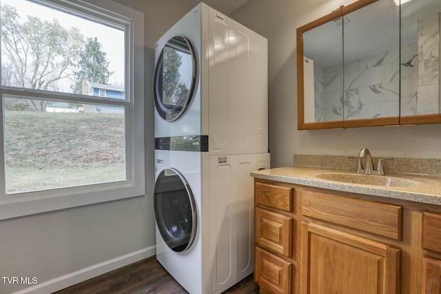 clothes washing area featuring plenty of natural light, a sink, stacked washer and clothes dryer, and baseboards