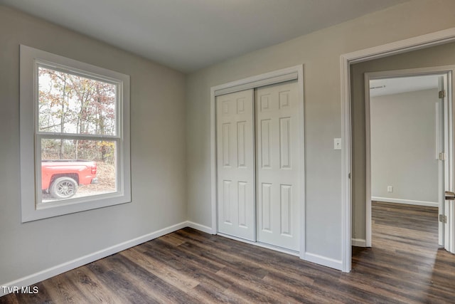 unfurnished bedroom with dark wood-style flooring, a closet, and baseboards