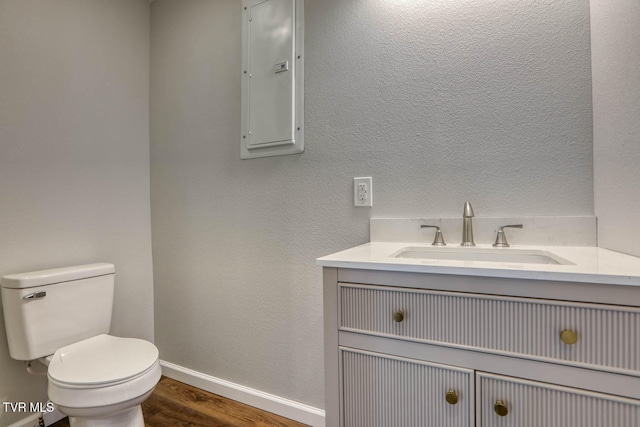 half bath featuring toilet, vanity, wood finished floors, electric panel, and baseboards