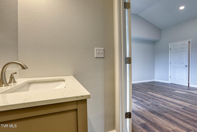 bathroom featuring lofted ceiling, a textured wall, wood finished floors, vanity, and baseboards