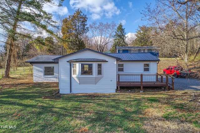 rear view of house with metal roof, a deck, a lawn, and a standing seam roof