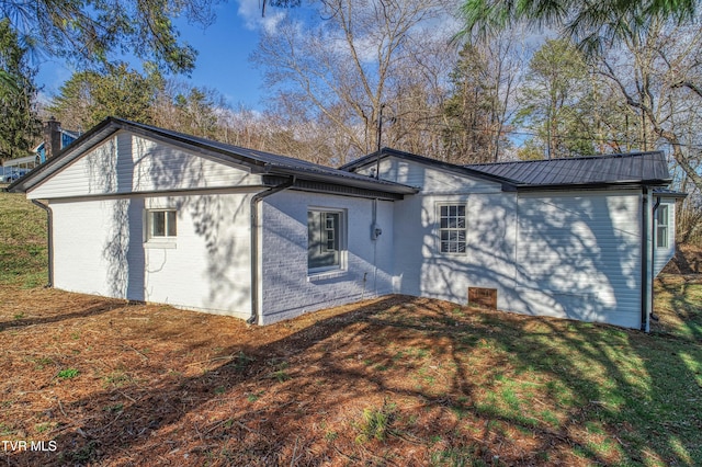 view of property exterior featuring metal roof, brick siding, and a lawn