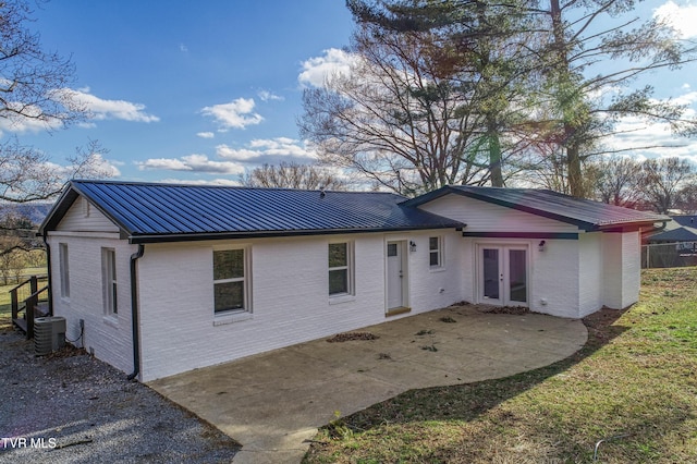 back of house featuring french doors, brick siding, metal roof, and central air condition unit