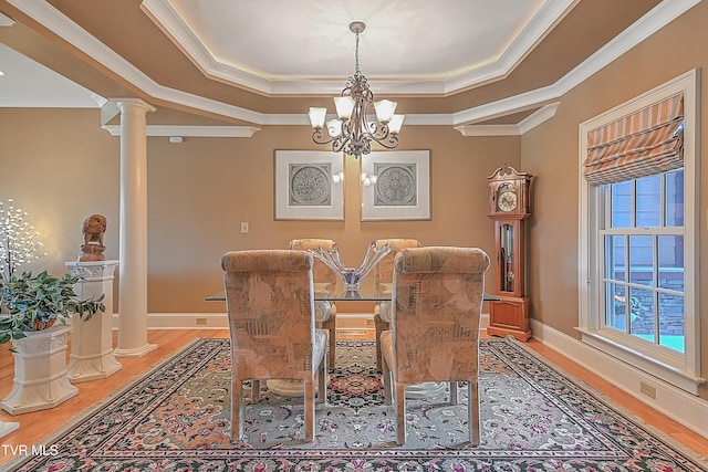 dining room featuring decorative columns, hardwood / wood-style flooring, crown molding, and a notable chandelier