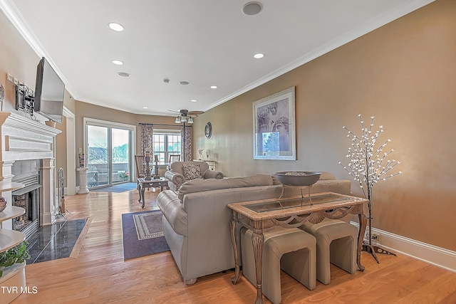 living room with a fireplace, light wood-type flooring, ceiling fan, and crown molding