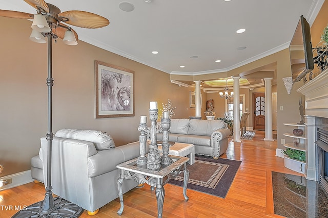 living room featuring wood-type flooring, ceiling fan with notable chandelier, decorative columns, and crown molding