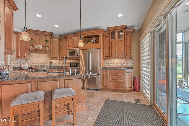 kitchen featuring dark stone counters, built in appliances, a breakfast bar, and hanging light fixtures