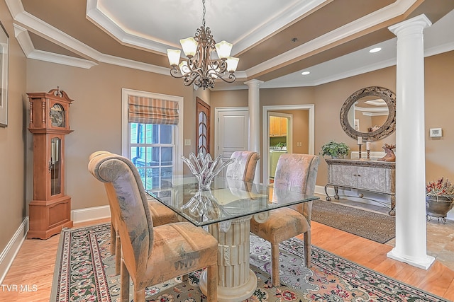 dining room featuring a chandelier, light wood-type flooring, crown molding, and decorative columns