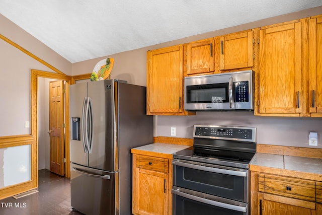 kitchen featuring tile countertops, vaulted ceiling, a textured ceiling, appliances with stainless steel finishes, and dark hardwood / wood-style flooring