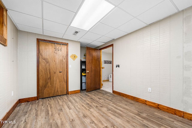 empty room with wooden walls, a drop ceiling, and light wood-type flooring