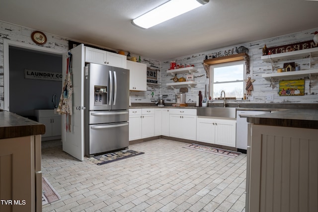 kitchen featuring wood counters, sink, stainless steel fridge, dishwashing machine, and white cabinetry