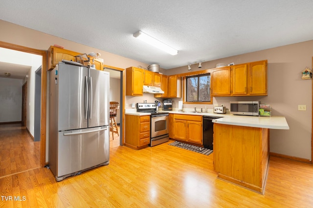 kitchen with light wood-type flooring, kitchen peninsula, a textured ceiling, and appliances with stainless steel finishes