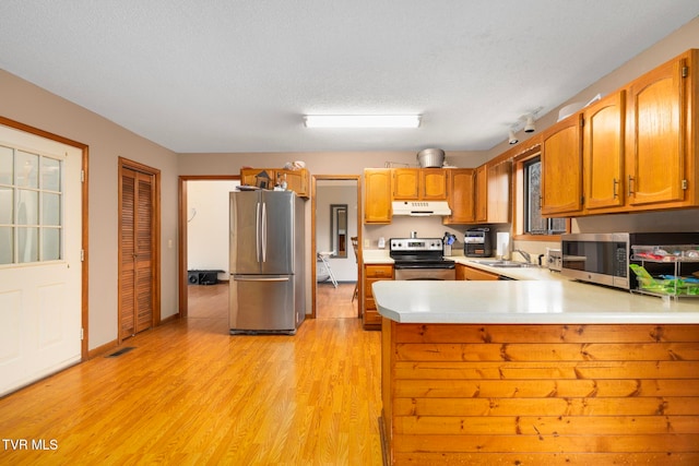 kitchen with kitchen peninsula, appliances with stainless steel finishes, a textured ceiling, sink, and light hardwood / wood-style floors