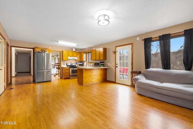 kitchen featuring kitchen peninsula, light hardwood / wood-style floors, a textured ceiling, a breakfast bar area, and appliances with stainless steel finishes