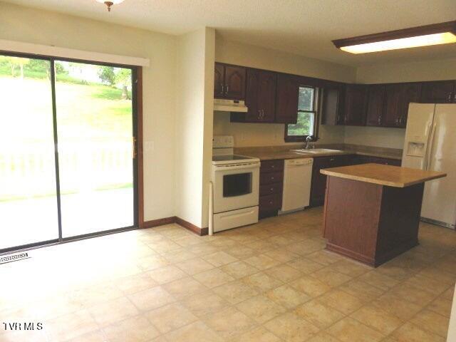 kitchen featuring dark brown cabinetry, sink, a kitchen island, and white appliances