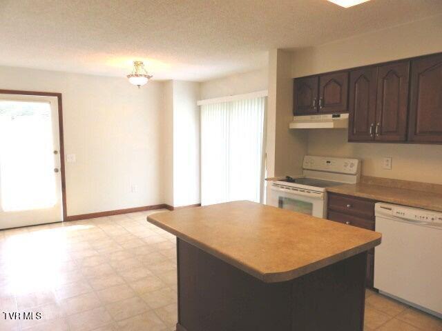 kitchen featuring a wealth of natural light, dark brown cabinets, a kitchen island, and white appliances