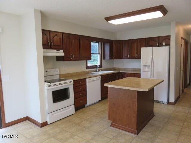 kitchen with dark brown cabinets, a center island, white appliances, and sink