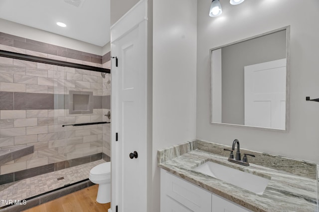 bathroom featuring vanity, wood-type flooring, a shower with shower door, and toilet