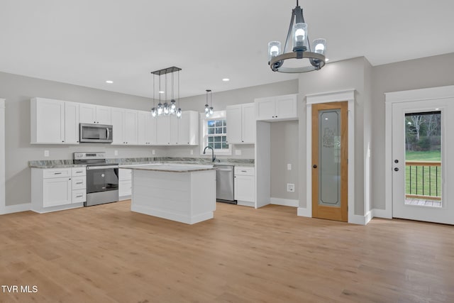 kitchen with pendant lighting, white cabinets, light wood-type flooring, a kitchen island, and stainless steel appliances