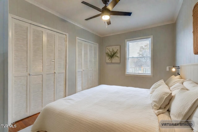 bedroom with ceiling fan, wood-type flooring, ornamental molding, and multiple closets