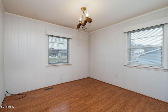 empty room with hardwood / wood-style flooring, ornamental molding, a wealth of natural light, and an inviting chandelier