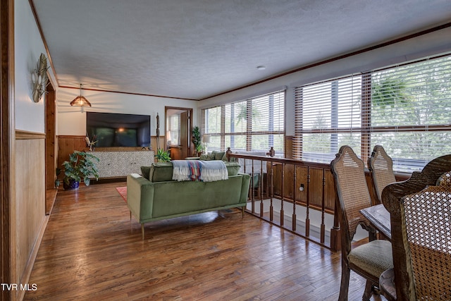 living room featuring hardwood / wood-style floors, a textured ceiling, ornamental molding, and wooden walls