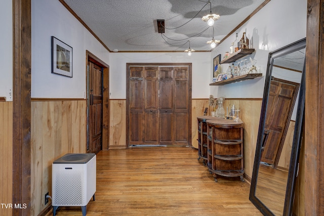 corridor featuring crown molding, light hardwood / wood-style flooring, a textured ceiling, and wooden walls