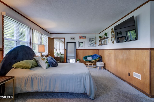 carpeted bedroom with wood walls, ornamental molding, and a textured ceiling