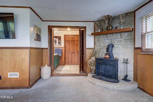 carpeted living room featuring a textured ceiling, a wood stove, wooden walls, and crown molding