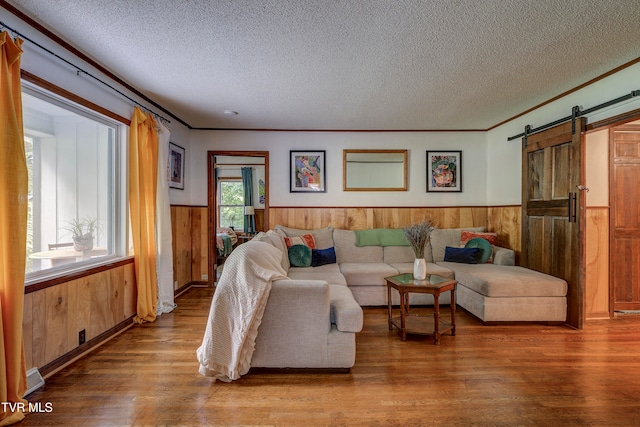 living room with hardwood / wood-style flooring, a barn door, crown molding, and a textured ceiling