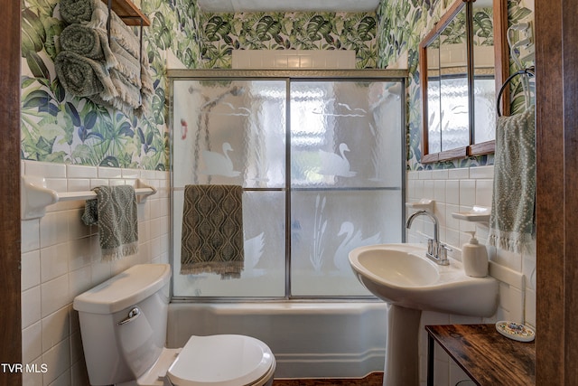 bathroom featuring toilet, tile walls, and bath / shower combo with glass door