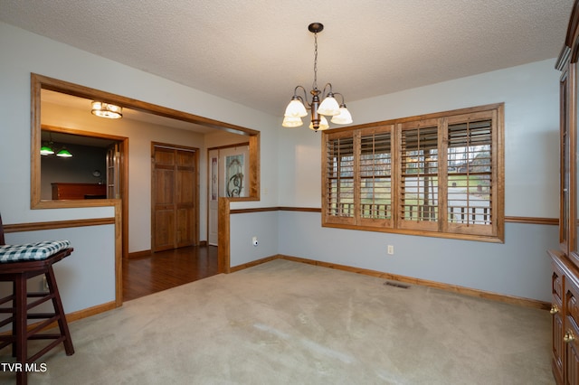 unfurnished dining area with carpet flooring, a textured ceiling, and a chandelier