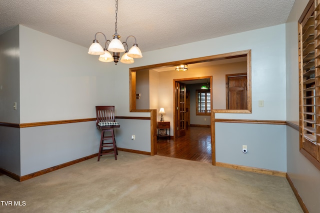 carpeted spare room featuring a textured ceiling and an inviting chandelier